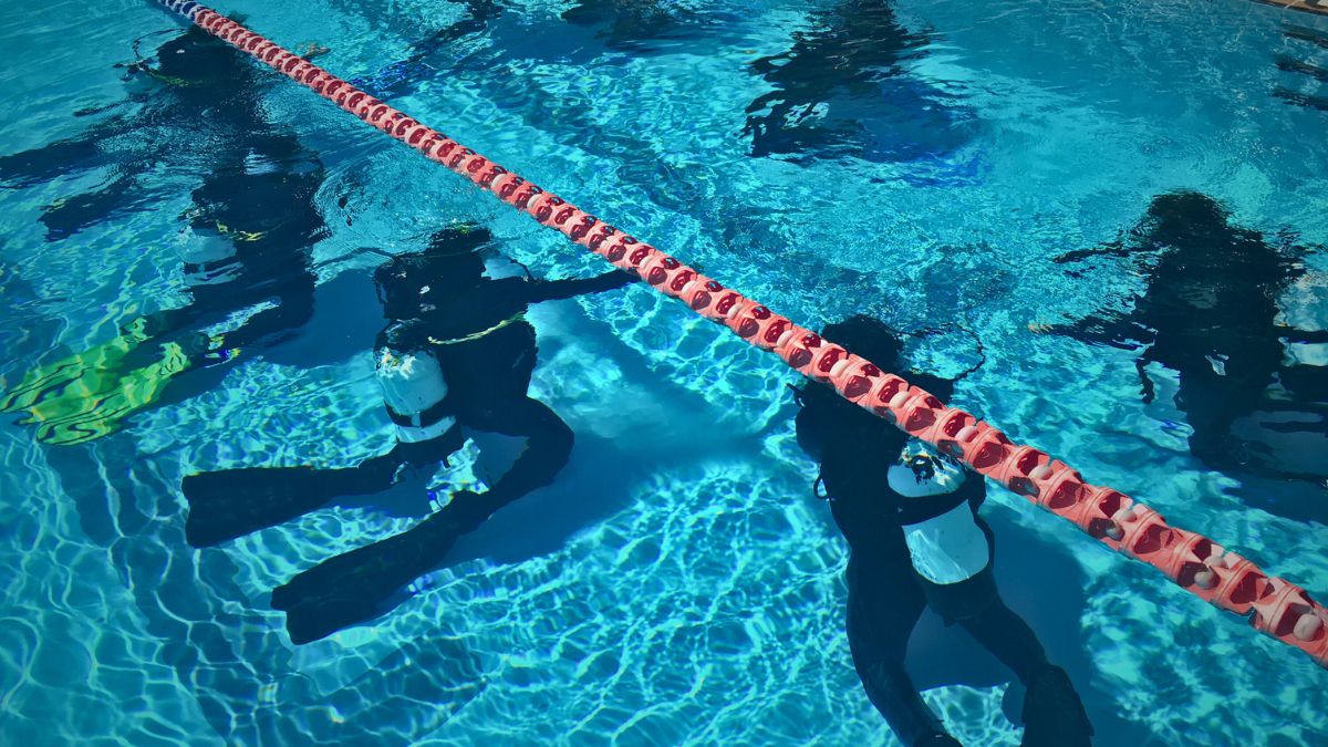 Scuba instructor explaining diving skills to two beginner students wearing full equipment but without regulators in mouths during pool training briefing in Costa Rica