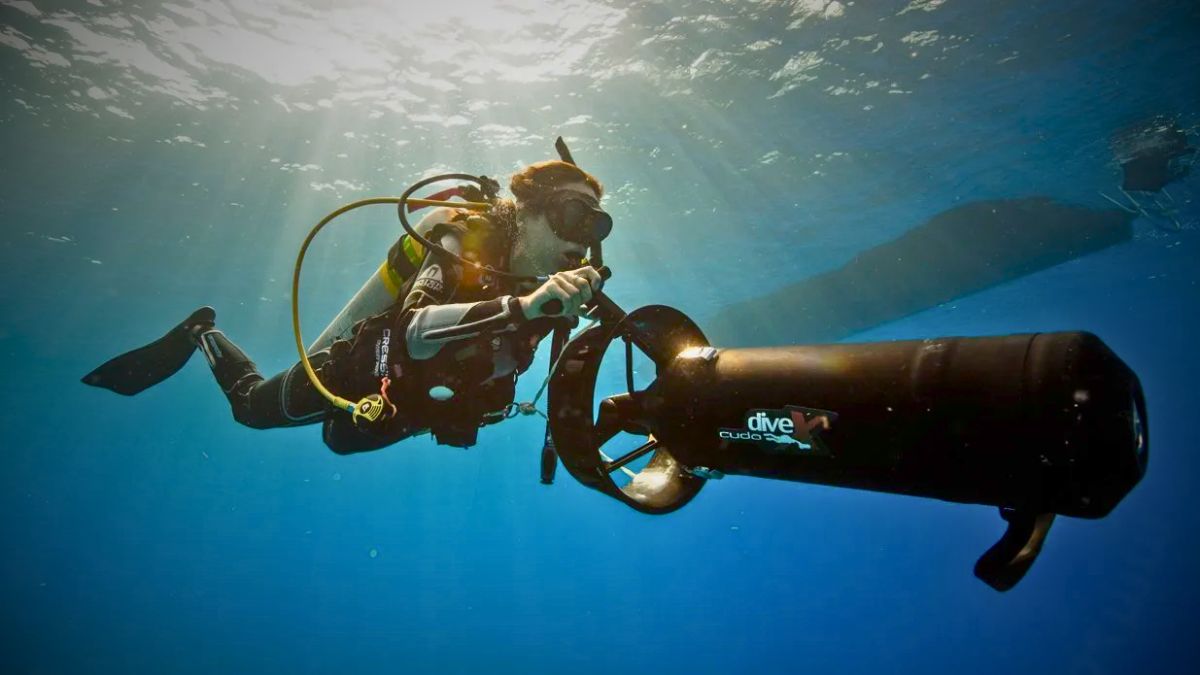 Scuba diver with regulator breathing riding underwater scooter DPV traveling through crystal clear Costa Rica waters showing diver propulsion vehicle in action