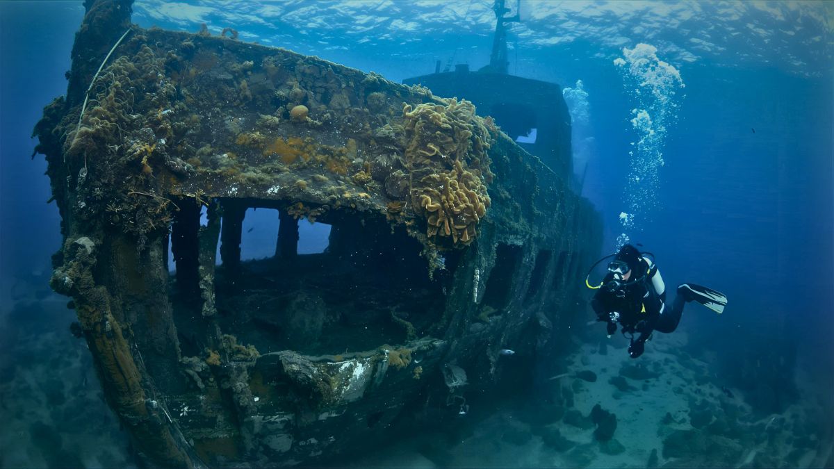 Scuba diver with regulator breathing exploring sunken shipwreck covered in marine life underwater in Costa Rica showing wreck diving specialty adventure
