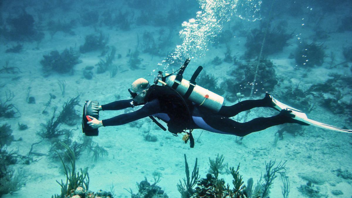 Underwater Scooter Guide: Everything About Diver Propulsion Vehicles (DPVs) » Costa Rica Divers Scuba diver gliding through clear tropical water with an underwater scooter DPV, surrounded by coral reef and marine life