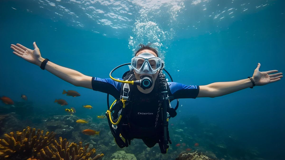 Joyful scuba diver with arms spread wide in freedom pose surrounded by colorful tropical fish in Costa Rica showing happiness and passion for diving lifestyle