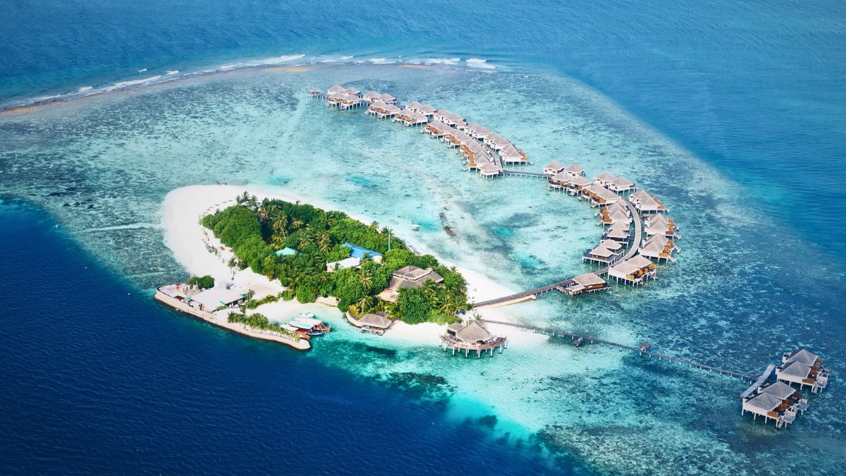 Is Scuba Diving in Maldives Worth It? Diver's Complete Guide » Costa Rica Divers Aerial view of a small Maldivian island with white sandy beaches, palm trees, and turquoise lagoon water surrounding it.