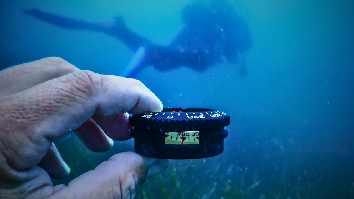 Underwater Navigation in Scuba Diving: How to Actually Find Your Way » Costa Rica Divers Scuba diver holding a compass underwater while swimming in a straight line over a sandy seabed