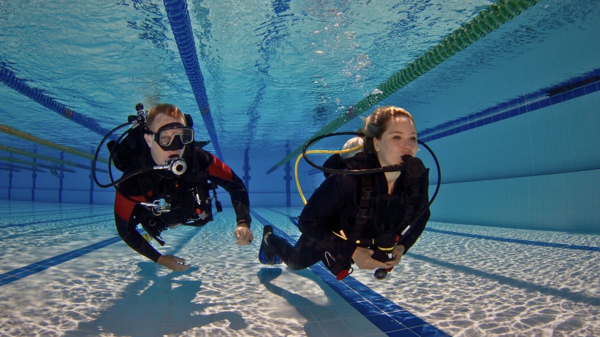 Beginner scuba diver giving OK signal underwater with instructor nearby in colorful coral reef Costa Rica showing complete introduction to diving
