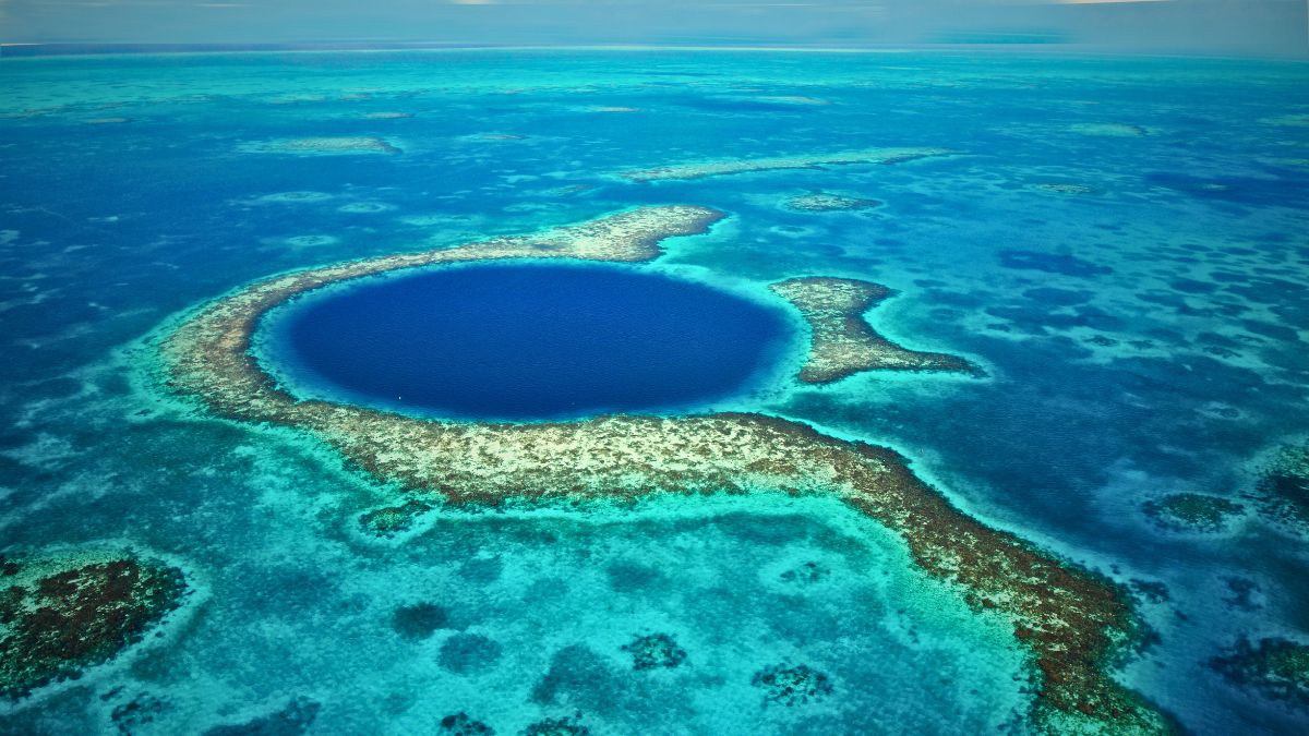 Aerial view of famous Great Blue Hole in Belize showing dramatic circular underwater sinkhole surrounded by turquoise coral reef with divers exploring