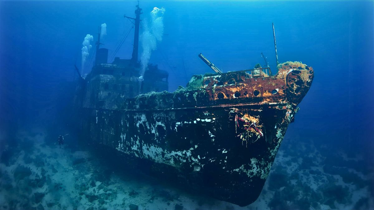 Scuba divers exploring dramatic sunken shipwreck covered in marine life in crystal clear European waters showing top wreck diving destination