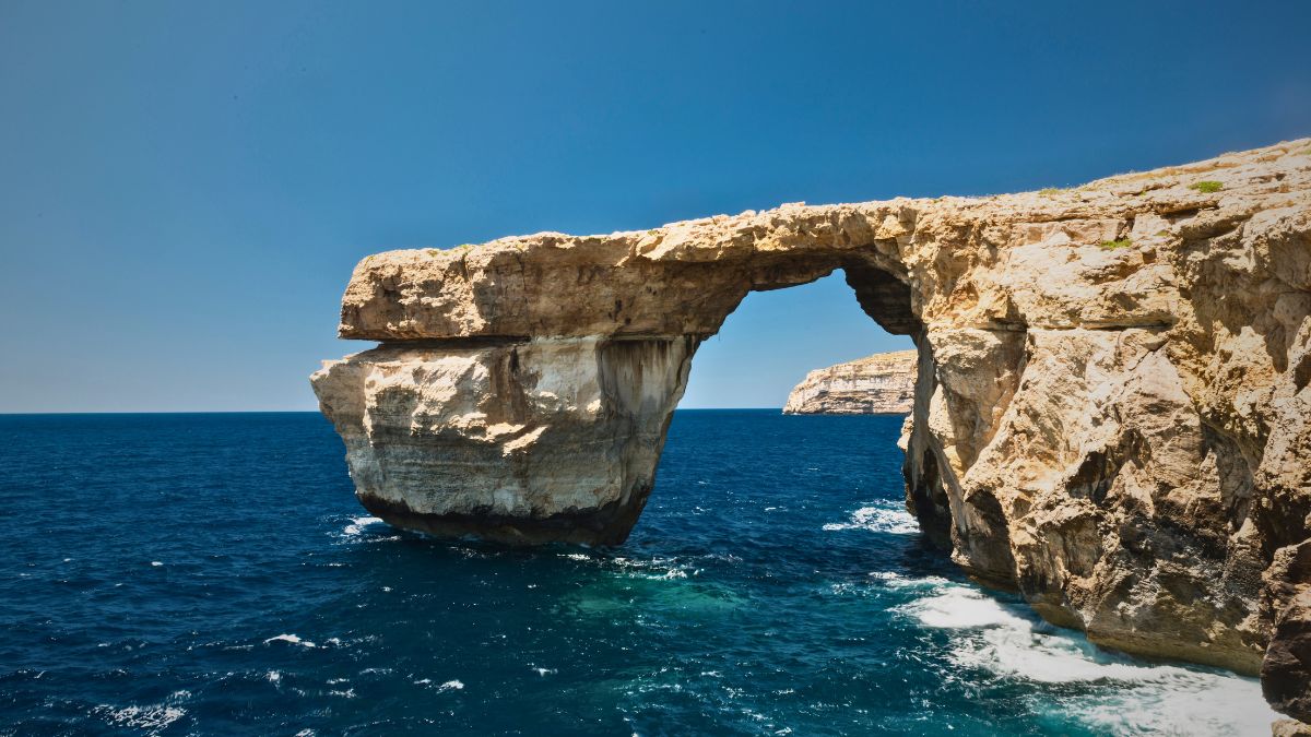 Scuba diver exploring dramatic underwater caves and rock formations with crystal clear water at famous Blue Hole dive site in Malta and Gozo