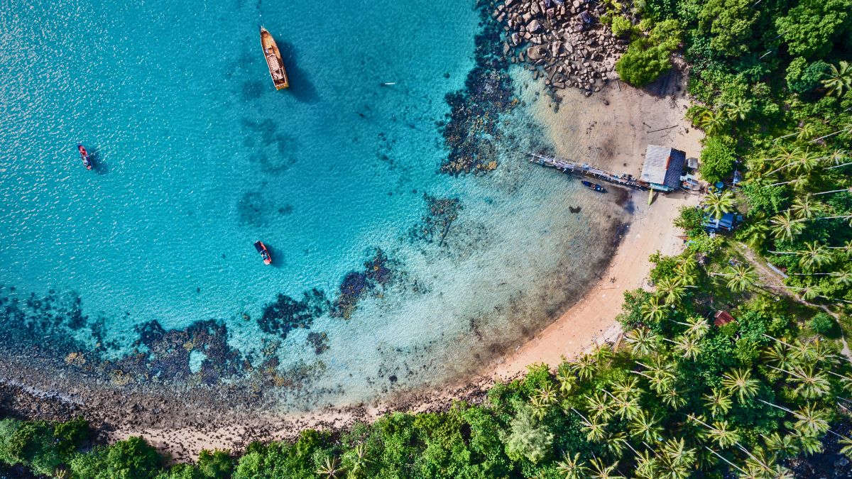 Traditional dhow boat anchored in crystal clear turquoise waters above coral reef with scuba divers exploring in Zanzibar Tanzania Indian Ocean