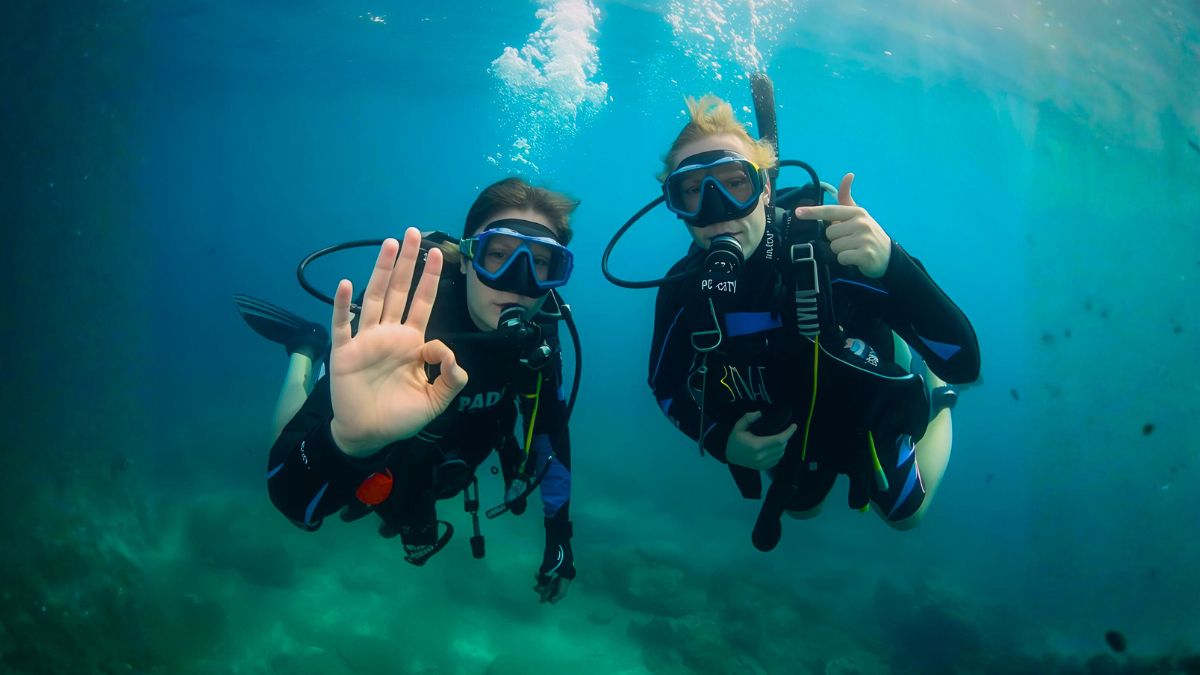 Scuba diving instructor teaching beginner student underwater during PADI certification course in crystal clear Costa Rican waters with tropical fish